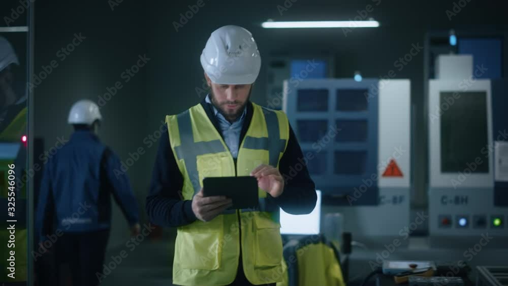 Poster professional engineer wearing safety vest and hardhat walks through modern factory workshop, uses di