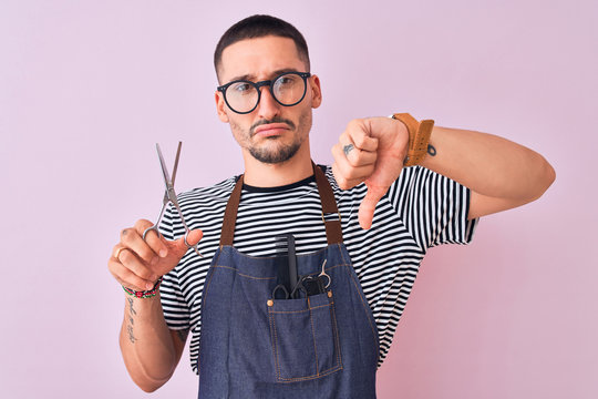 Young handsome hairdresser man wearing apron over pink isolated background with angry face, negative sign showing dislike with thumbs down, rejection concept