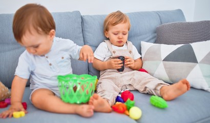 Beautiful toddlers, one of them crying, sitting on the sofa playing with toys at home