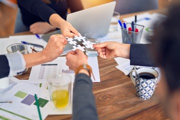 Group of business workers with hands together connecting pieces of puzzle at the office