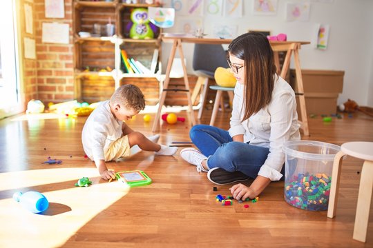 Beautiful teacher and toddler drawing using digital board around lots of toys at kindergarten