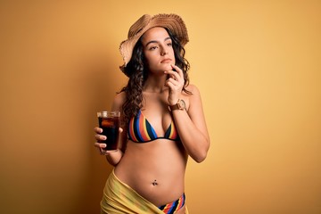 Young beautiful woman with curly hair on vacation wearing bikini drinking cola beverage serious...