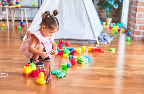Young beautiful toddler sitting on the floor playing with small cars toys at kindergaten