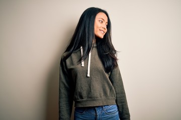 Young beautiful chinese sporty woman wearing sweatshirt over isolated white background looking away to side with smile on face, natural expression. Laughing confident.