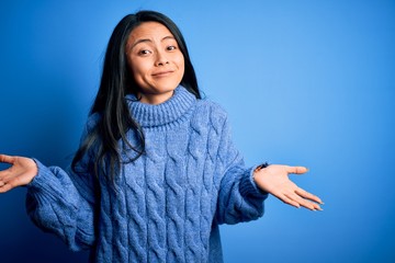 Young beautiful chinese woman wearing casual sweater over isolated blue background clueless and...