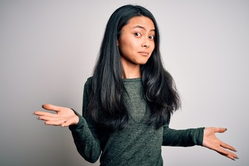 Young beautiful chinese woman wearing casual t-shirt over isolated white background clueless and confused expression with arms and hands raised. Doubt concept.