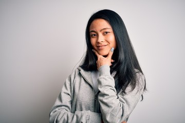 Young beautiful chinese sporty woman wearing sweatshirt over isolated white background looking confident at the camera smiling with crossed arms and hand raised on chin. Thinking positive.