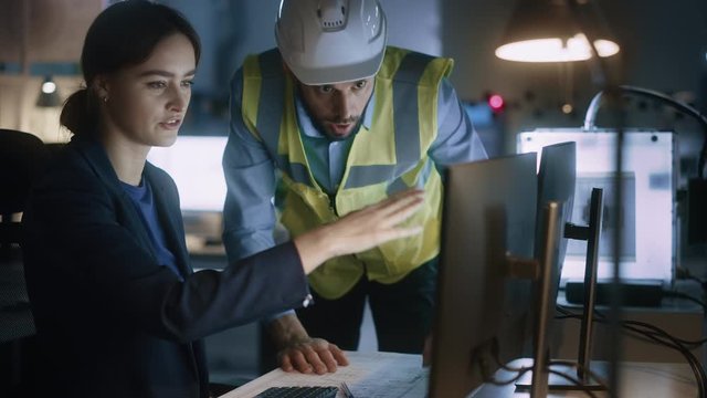 Modern Factory Office: Male Project Manager Talks to a Female Industrial Engineer who Works on Computer. Professional Teamwork, Specialists Solving Problems, Finding Solutions