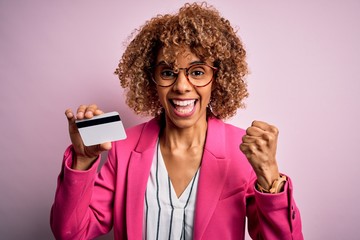 Young african american business woman holding id card identification over pink background screaming...
