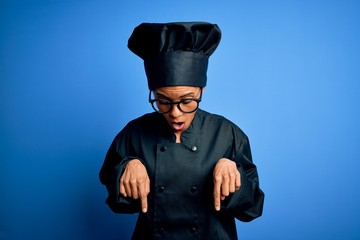Young african american chef woman wearing cooker uniform and hat over blue background Pointing down with fingers showing advertisement, surprised face and open mouth
