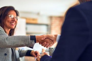 Two middle age business workers smiling happy and confident. Working together with smile on face shaking hands at the office