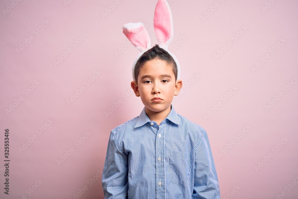 Sticker young little boy kid wearing easter bunny ears over isolated pink background with serious expression