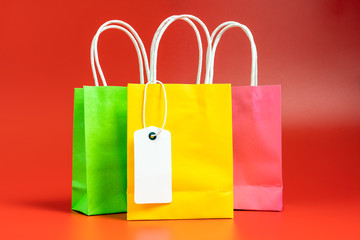 Yellow, green and pink gift or shopping bags with blank tag isolated on red background