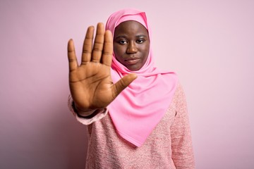 Young african american plus size woman wearing muslim hijab over isolated pink background doing...