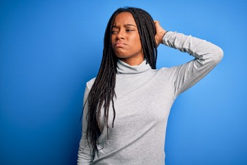 Young african american woman standing wearing casual turtleneck over blue isolated background confuse and wondering about question. Uncertain with doubt, thinking with hand on head. Pensive concept.
