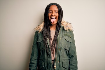 Young african american woman wearing winter parka coat over isolated background sticking tongue out happy with funny expression. Emotion concept.