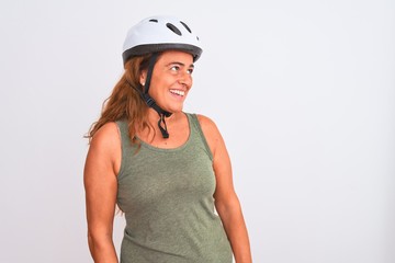 Middle age mature cyclist woman wearing safety helmet over isolated background looking away to side with smile on face, natural expression. Laughing confident.