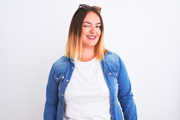 Beautiful woman wearing denim shirt standing over isolated white background winking looking at the...