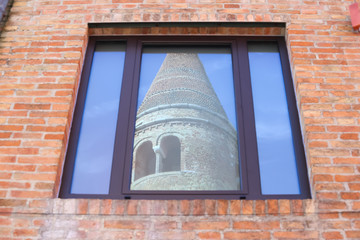 caorle, italy, 02/16/2020 , Detail of Duomo's belltower reflection from town hall's windows, in the historical city center of caorle, a little town on the Italian coast of adriatic sea .