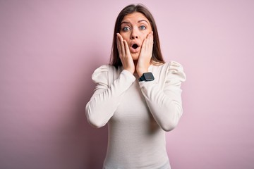 Young beautiful woman with blue eyes wearing casual white t-shirt over pink background afraid and shocked, surprise and amazed expression with hands on face