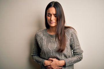 Young beautiful brunette woman wearing casual sweater over isolated white background with hand on stomach because indigestion, painful illness feeling unwell. Ache concept.