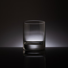 Empty transparent glass on a dark background, reflected from a black surface