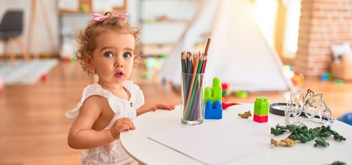 Beautiful caucasian infant playing with toys at colorful playroom. Happy and playful drawing with...