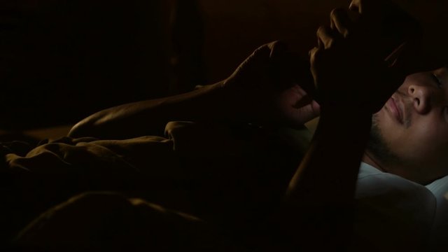 Young man using a smartphone in his bed at night .