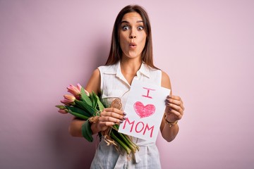 Beautiful woman celebrating mothers day holding love mom message and bouquet of tulips scared in shock with a surprise face, afraid and excited with fear expression