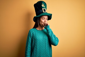 Young beautiful brunette woman wearing green hat with clover celebrating saint patricks day feeling unwell and coughing as symptom for cold or bronchitis. Health care concept.