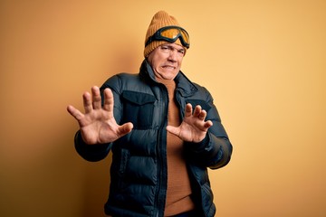Middle age handsome grey-haired skier man on vacation wearing ski goggles disgusted expression,...