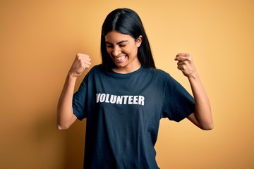 Young beautiful hispanic woman wearing volunteer t-shirt as social charity moral very happy and excited doing winner gesture with arms raised, smiling and screaming for success. Celebration concept.