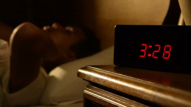 Depressed man suffering from insomnia lying in bed at night .