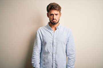 Young handsome man with beard wearing striped shirt standing over white background depressed and worry for distress, crying angry and afraid. Sad expression.