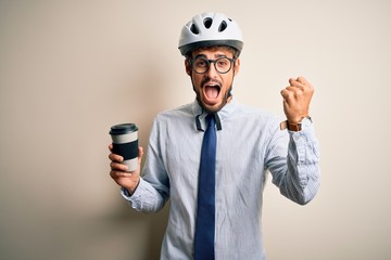 Young businessman wearing glasses and bike helmet drinking cup of coffee screaming proud and celebrating victory and success very excited, cheering emotion