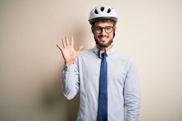 Young businessman wearing glasses and bike helmet standing over isolated white bakground showing and pointing up with fingers number five while smiling confident and happy.