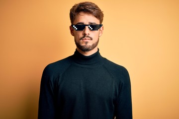 Young man wearing thug life fanny sunglasses standing over isolated yellow background with serious...