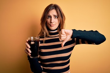 Young beautiful brunette woman drinking glass with cola refreshment using straw with angry face,...
