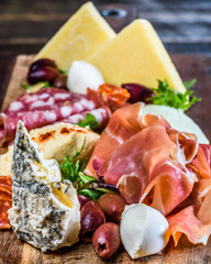 A serving of Italian Antipasto on a wooden chopping board consisting of sliced meats, cheese and olives.
