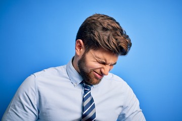Young blond businessman with beard and blue eyes wearing elegant shirt and tie standing with hand on stomach because nausea, painful disease feeling unwell. Ache concept.