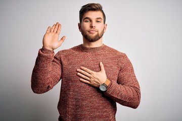 Young blond man with beard and blue eyes wearing casual sweater over white background Swearing with...