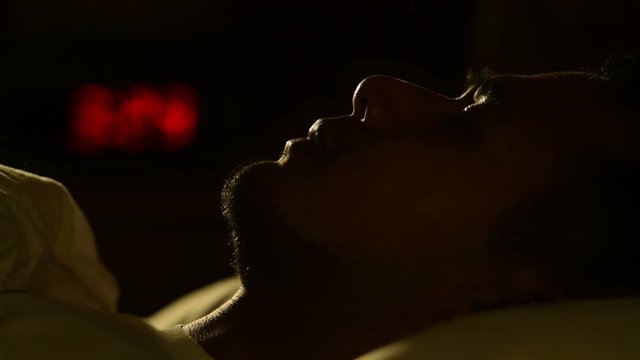 Depressed man suffering from insomnia lying in bed at night .