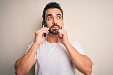 Young handsome man with beard having conversation talking on the smartphone serious face thinking...