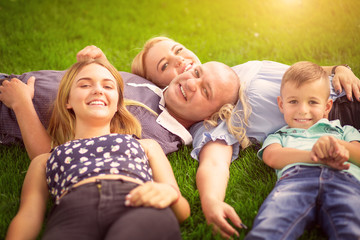 Happy family concept. Mother, father, sun and daughter outdoors lying on grass loan sun flare on right in a sunny day.
