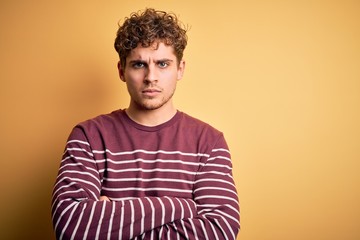 Young blond handsome man with curly hair wearing casual striped sweater skeptic and nervous,...