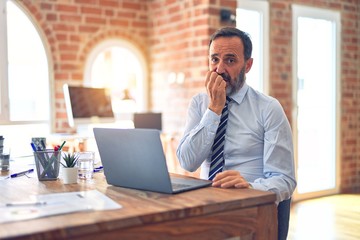 Middle age handsome businessman wearing tie sitting using laptop at the office looking stressed and nervous with hands on mouth biting nails. Anxiety problem.