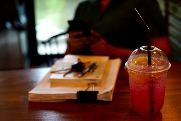 Plakat Red sweetened water mixed with soda and lemon is cool drink in a clear plastic glass placed next to the document.The front of the woman who is texting on a mobile phone.