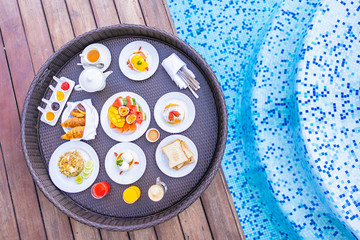 Flotaing breakfast tray around outdoor swimming pool with bread fruit egg coffee and juice