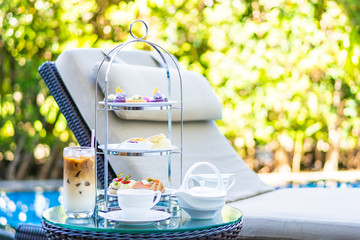 Afternoon tea set with latte coffee and hot tea on table neary chair around swimming pool