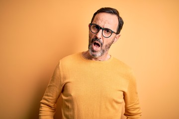 Obraz premium Middle age hoary man wearing casual sweater and glasses over isolated yellow background In shock face, looking skeptical and sarcastic, surprised with open mouth